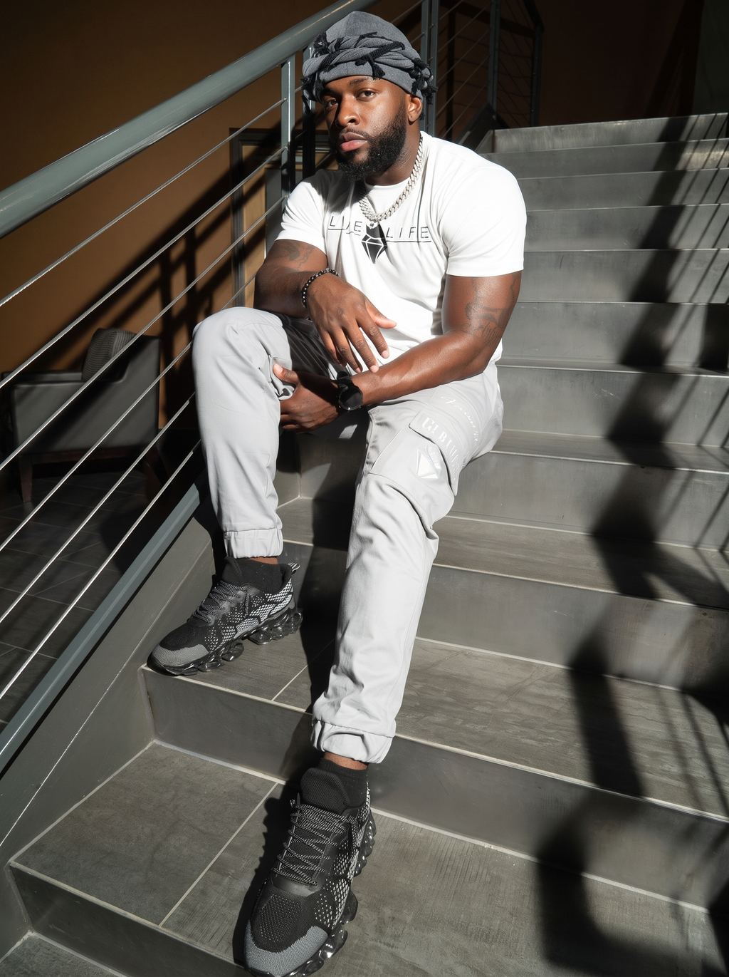 Man wearing the charcoal grey twist turban, seated on stairs in streetwear